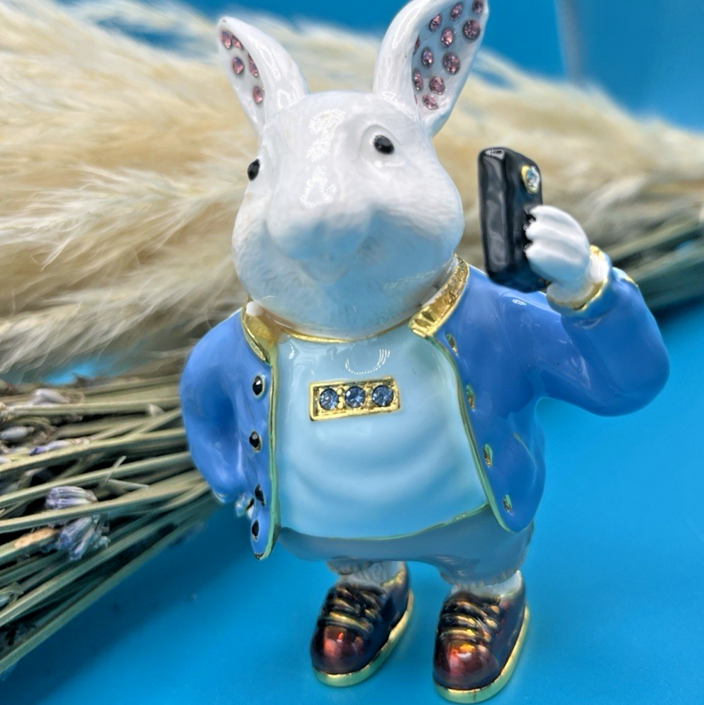 Decorative figurine of a rabbit in a blue outfit holding a smartphone on a blue background