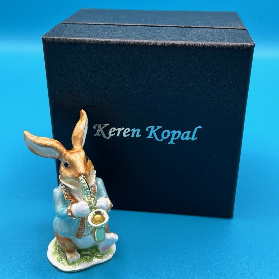 Decorative rabbit figurine with a saxophone in front of a Keren Kopal box on a blue background