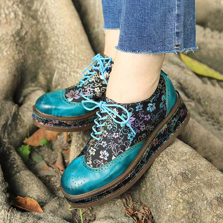 Blue floral-patterned shoes worn with blue jeans on a stone surface.