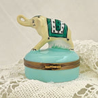 Decorative elephant box with a green patterned cloth on a light blue base, placed on a textured white surface.
