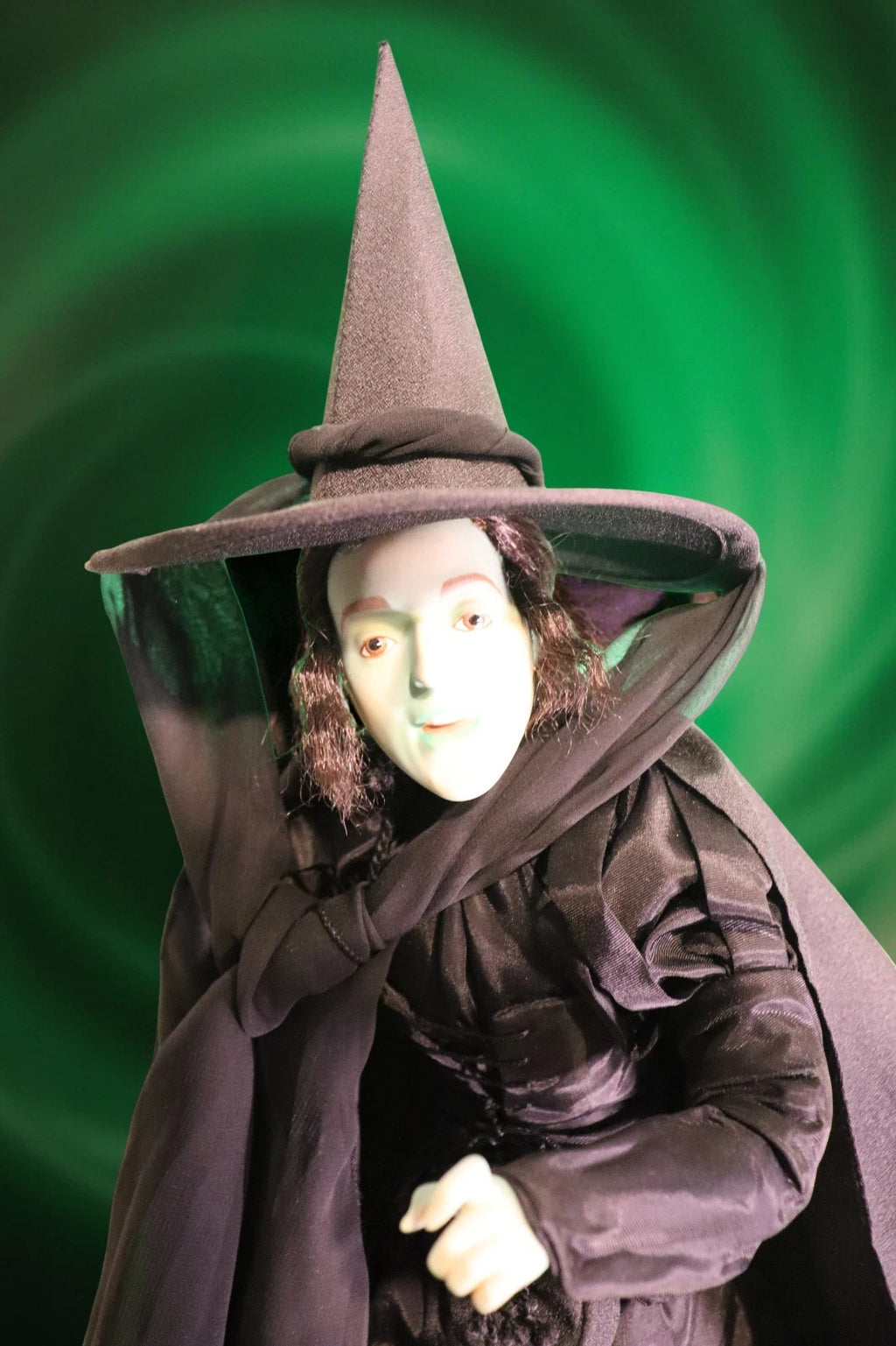 Person wearing a witch costume with a pointed hat and cloak against a green swirling background