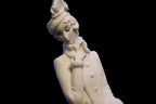 White ceramic sculpture of a seated figure on a black background