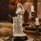 White figurine of a woman with a dove on a wooden base, surrounded by candles and books.