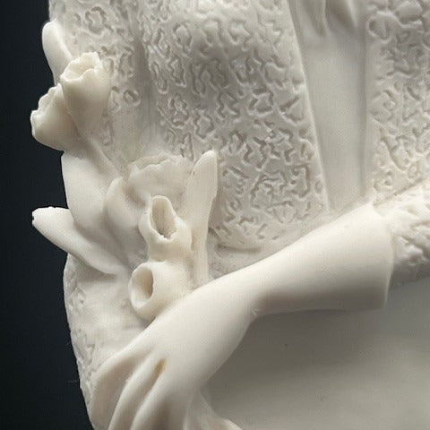 Close-up of a white ceramic sculpture with intricate detailing on a dark background