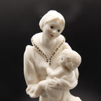 White ceramic figurine of a woman holding a child against a black background