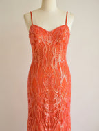 Orange sequin evening gown with intricate pattern on a mannequin against a beige background