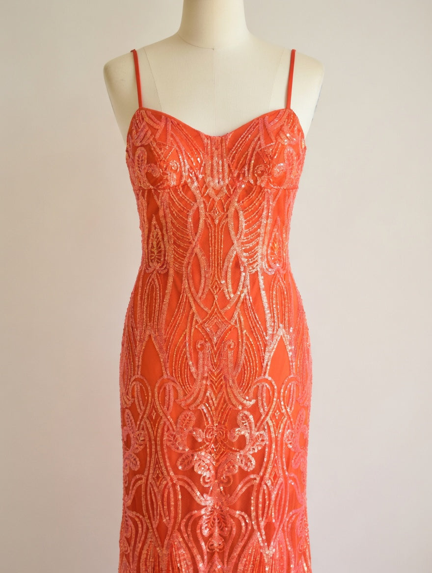 Orange sequin evening gown with intricate pattern on a mannequin against a beige background