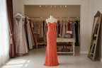 Orange evening gown on a mannequin against a beige wall.