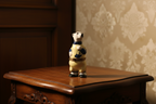 Small figurine of a bear in a sweater on a wooden surface with patterned wallpaper in the background