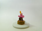 Small figurine of a person in a pink outfit on a white base with a white background