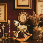 Decorative room with a rocking horse, framed pictures, and candles on a dark surface.