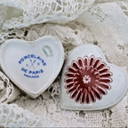 Top and bottom of heart-shaped porcelain trinket box on a lace background, one with 'Porcelaine de Paris France' text and the other with a floral design.