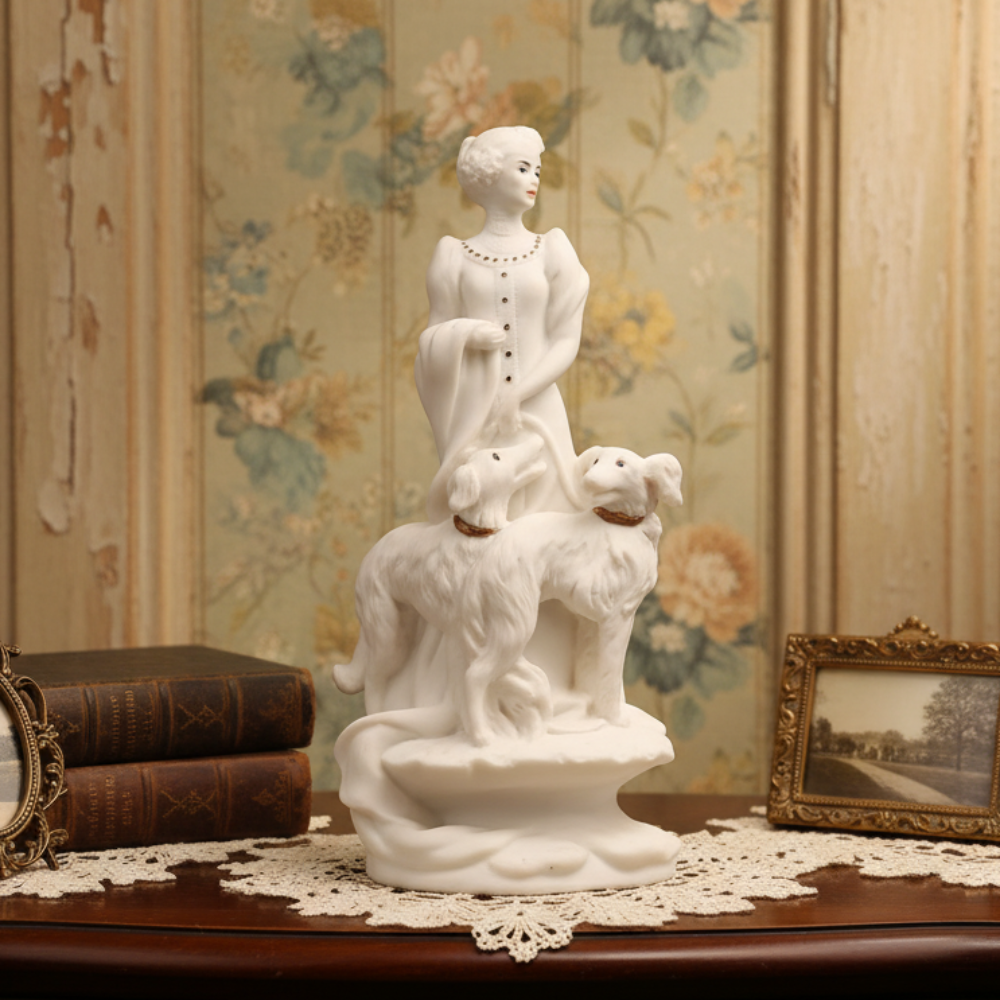 White marble sculpture of a woman with two dogs on a wooden table with floral wallpaper.