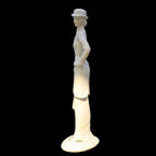 White ceramic figurine of a woman wearing a hat on a black background