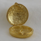 Gold locket with intricate design on a white background